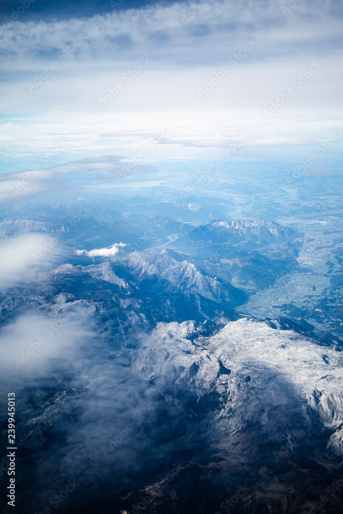 Airplane window view on a blue landscape with mountains and clouds