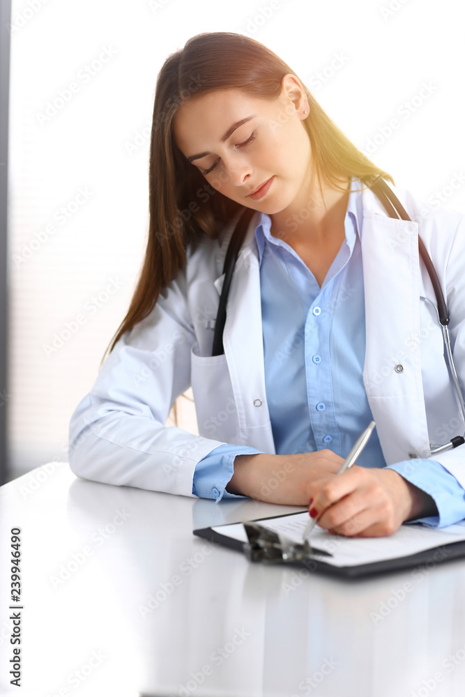 Doctor woman filling up medical form while sitting at the desk in hospital office. Physician at work. Medicine and health care concept Doctor woman filling up medical form while sitting at the desk in hospital office. Physician at work. Medicine and health care concept