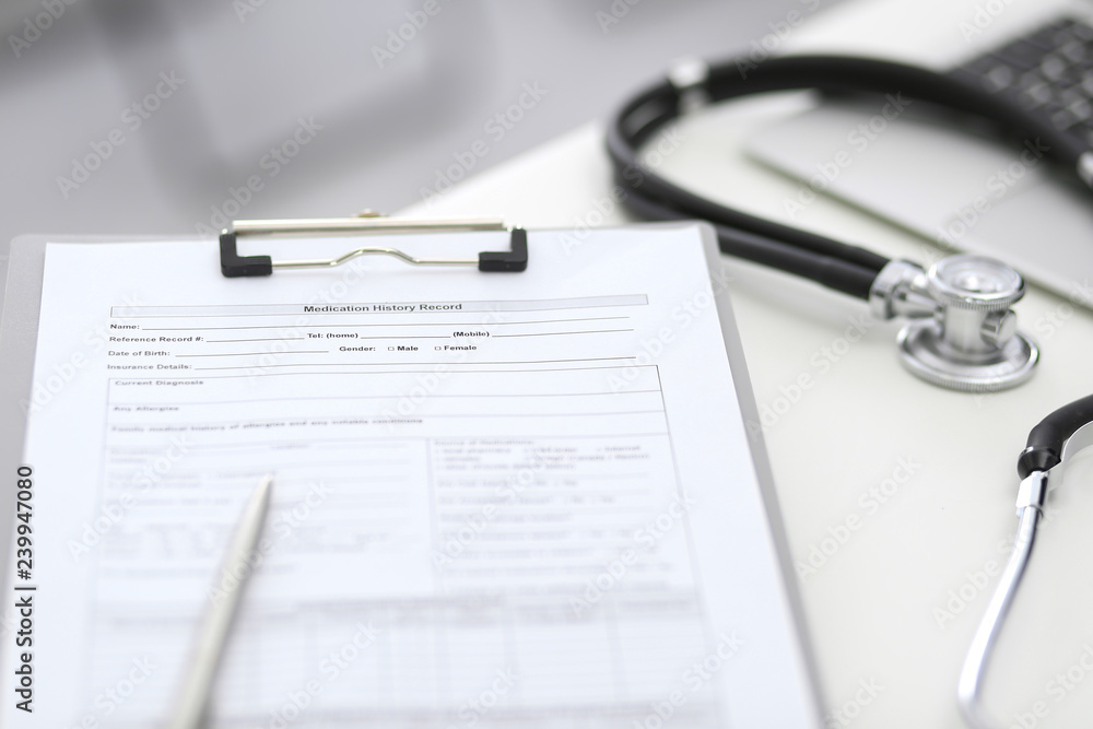 Stethoscope, clipboard with medical form lying on hospital reception desk with laptop computer. Medical tools at doctor working table.Medicine and health care concept Stethoscope, clipboard with medical form lying on hospital reception desk with laptop computer. Medical tools at doctor working table.Medicine and health care concept