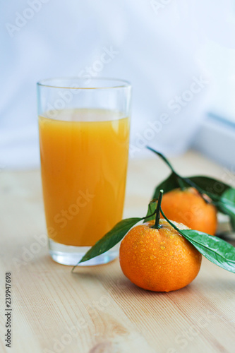 a glass of fresh orange juice and tangerines next to a wooden background. appetizing and fresh.close up