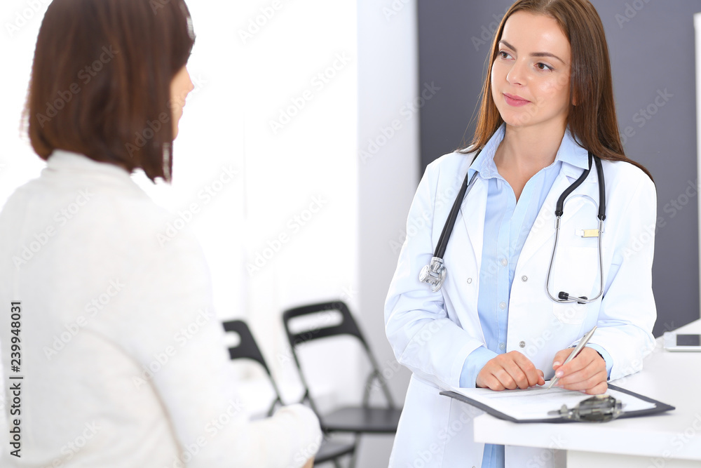 Doctor and patient discussing something while standing near reception desk in emergency hospital. Physician at work in clinic. Medicine and health care concept Doctor and patient discussing something while standing near reception desk in emergency hospital. Physician at work in clinic. Medicine and health care concept