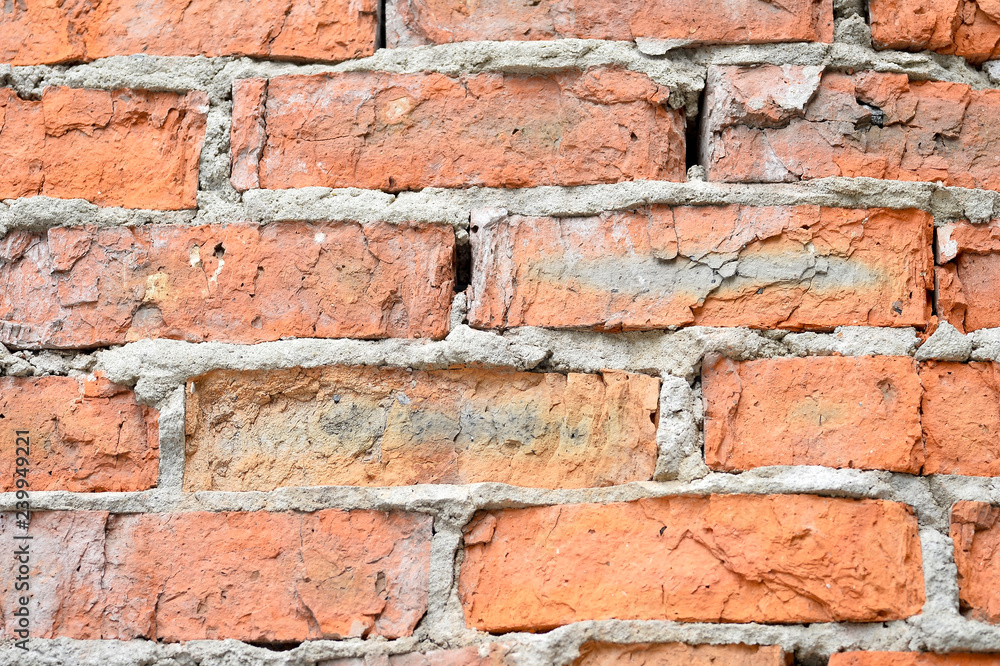 Fototapeta premium The destroyed wall of red brick with the remains of concrete solution close up. Texture rough, background