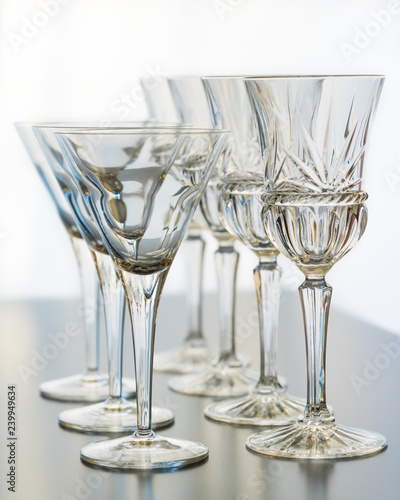 Wine and martini glasses set up in verticle rows on a reflective table top.