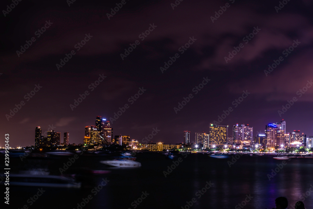 Fototapeta premium Beautiful night sky with skyscrapers in Jomtien beach Pattaya, Thailand, Crowd of people are relax on the beach in the night, Tourist are walking on the beach with cool wind air from sea