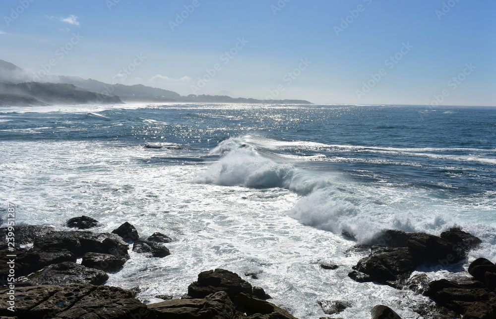 Big waves from a cliff. Rocks, wild sea with foam and mist. Blue sky, sunny day, Galicia, Spain.