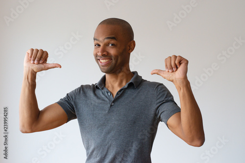 Cheerful Afro American guy proud of himself. Smiling young black man pointing thumbs at himself. Self promotion concept photo