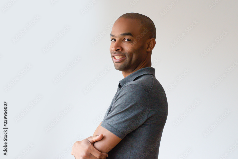 Positive mix raced guy posing with arms folded. Side view of young black man turning face to camera and smiling. Side portrait concept Positive mix raced guy posing with arms folded. Side view of young black man turning face to camera and smiling. Side portrait concept