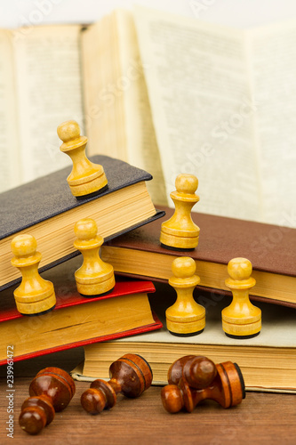 White chess pieces placed on books above defeated black pawns on wooden table revealing concept of race discrimination  photo