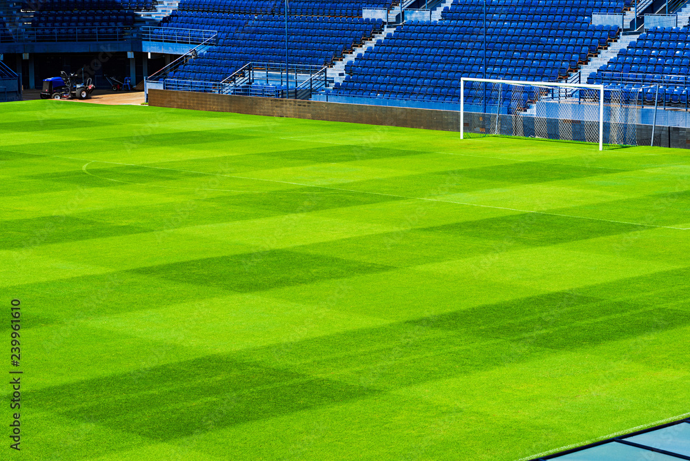 Fototapeta premium Green soccer field with blue seats and lawn mower