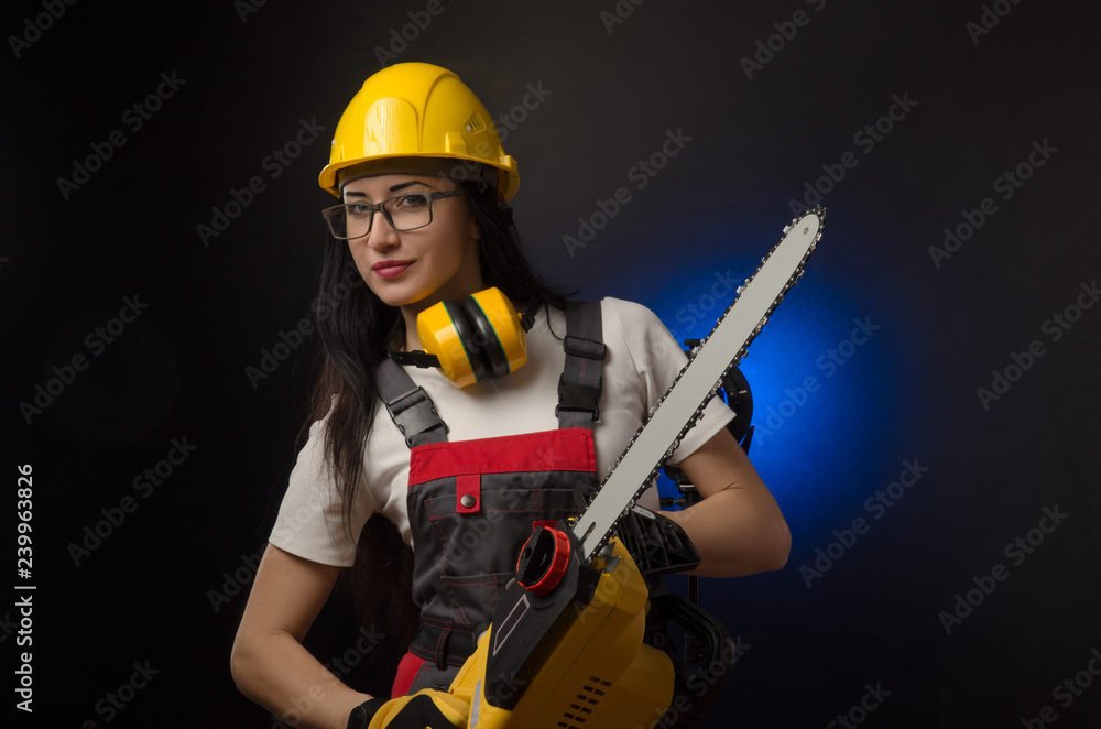 brunette girl in special clothes and a worker in a helmet posing on a black background with a working tool