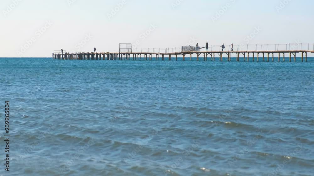 People are walking on old wooden pier in the sea. Side view. People are walking on old wooden pier in the sea. Side view.