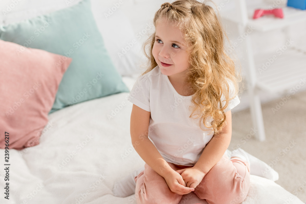 high angle view of adorable kid sitting on bed in children room and looking away high angle view of adorable kid sitting on bed in children room and looking away