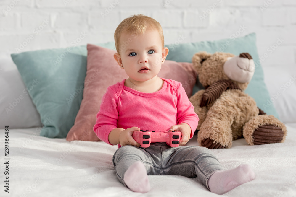 adorable child in pink shirt holding pink joystick on bed in children room adorable child in pink shirt holding pink joystick on bed in children room