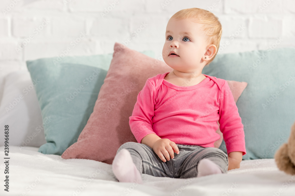 adorable kid sitting on bed with pillows and looking up in children room adorable kid sitting on bed with pillows and looking up in children room