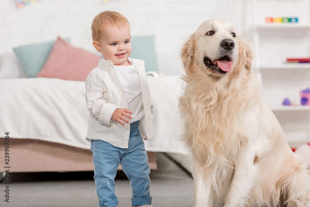 smiling adorable kid looking at golden retriever dog in children room