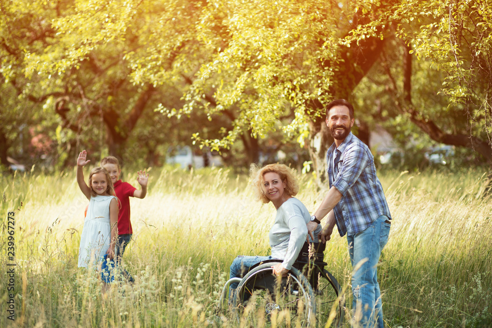 Woman in wheelchair wirh her family is looking back and waves Woman in wheelchair wirh her family is looking back and waves