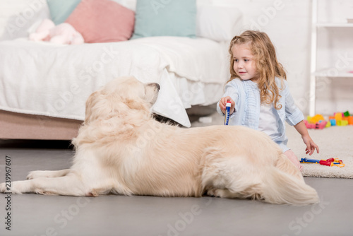 adorable child pretending veterinarian and examining golden retriever in children room