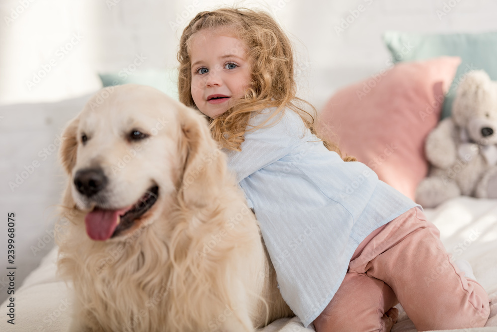adorable kid and cute dog lying on bed in children room, looking at camera adorable kid and cute dog lying on bed in children room, looking at camera