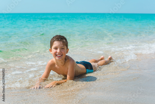 A cheerful kid on the beach lies in the clear sea water.
