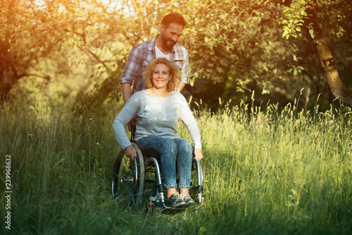 Принти на полотні Smiling woman in wheelchair with husband in the park on sunny day