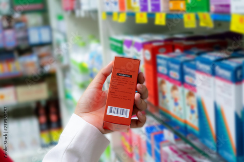 Pharmacist scanning price on a red medicine box with barcode reader in pharmacy store