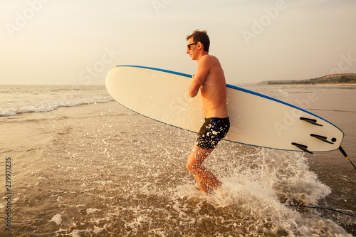 Photography male athlete surfer running to the sea with surf board sunset at the beach tropical paradise beach