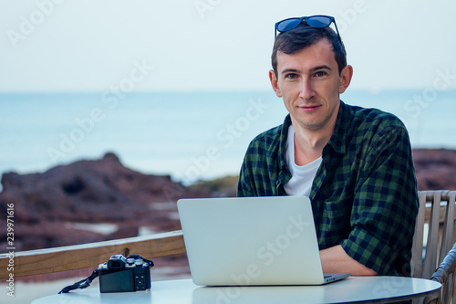 remote work surfing and freelance vacation. Young freelancer surfer businessman working laptop computer on the tropical beach in the summer cafe on the street veranda.man vacation in exotic country