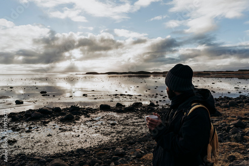 Anonymous tourist with cup of coffee against lake in Iceland