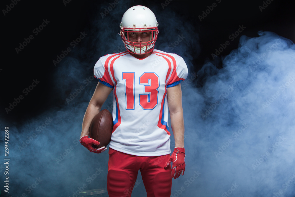 Front view portrait of american football player wearing helmet with ball against white smoke