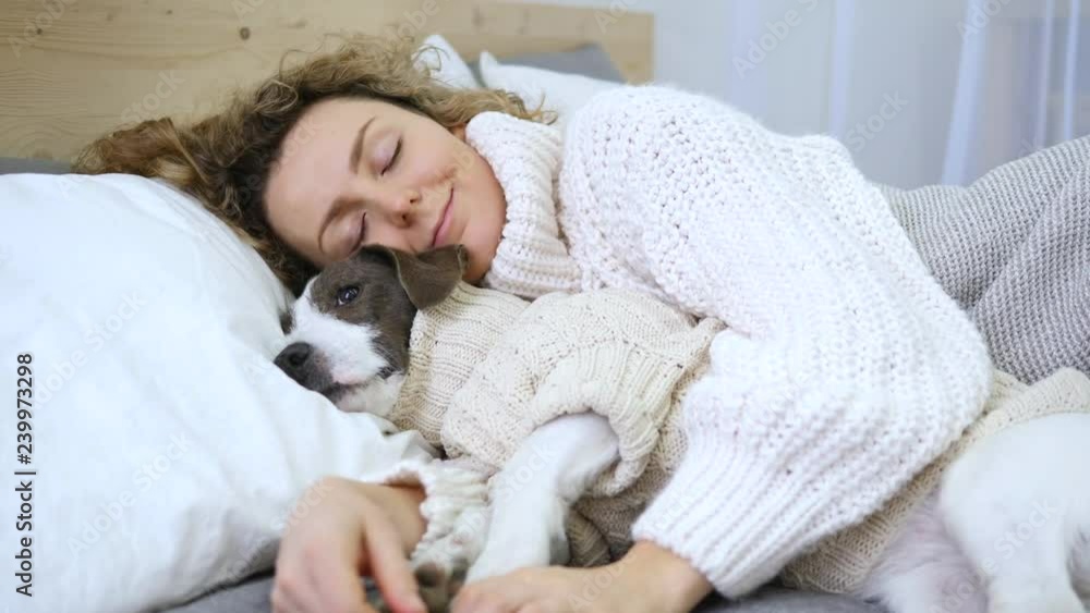 Smiling Woman Sleeping With Her Dog In Bed Wearing Cozy Knitted Sweaters. Smiling Woman Sleeping With Her Dog In Bed Wearing Cozy Knitted Sweaters.