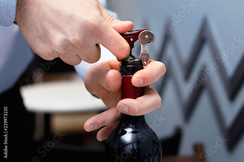 sommelier is opening a bottle of wine with a corkscrew