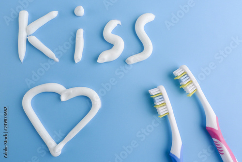 A heart and a text made with white toothpaste on blue. The word KISS and a heart on blue. Toothpaste shapes and toothbrushes on blue.