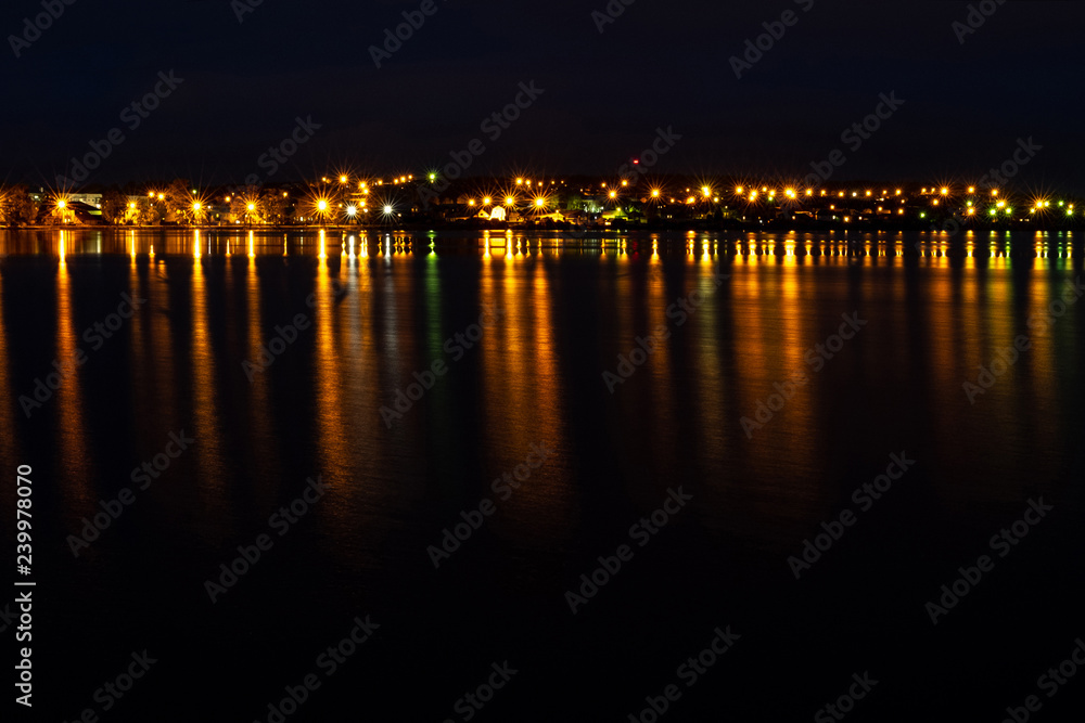 city lights are reflected on the water surface, a narrow line of light on the horizon