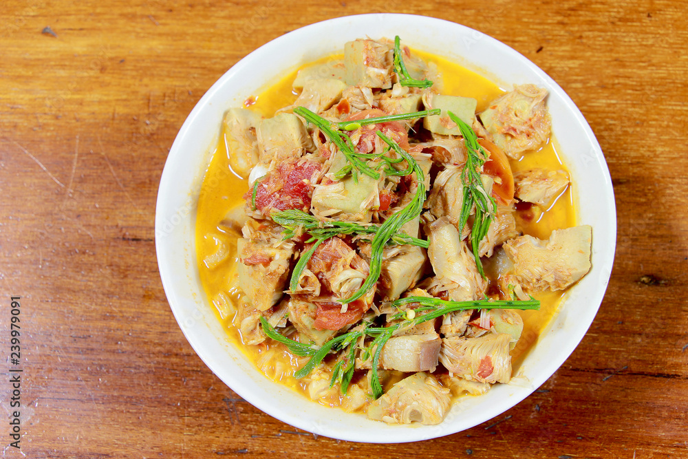 Northern Thailand local food called Kaeng Khanun-on is cooking like a young jack fruit soup with pork spare rib Thai herb, Climbing Wattle, Acacia pennata, red eggplant in white bowl on wooden table. Northern Thailand local food called Kaeng Khanun-on is cooking like a young jack fruit soup with pork spare rib Thai herb, Climbing Wattle, Acacia pennata, red eggplant in white bowl on wooden table.