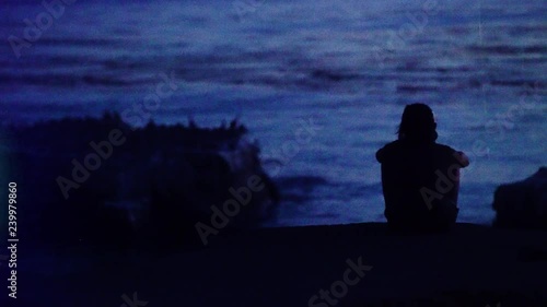 Faux Super 8mm: Silhouetted man rests on cliff next to ocean, contemplating