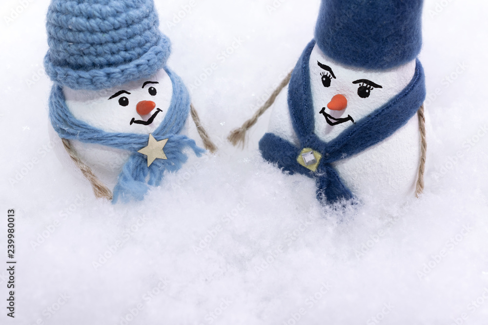 Two snowmen in a blue hat and scarf are standing in a snowdrift of snow. Two snowmen in a blue hat and scarf are standing in a snowdrift of snow.