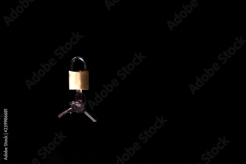 Iron lock, golden color with keys, on a black background.