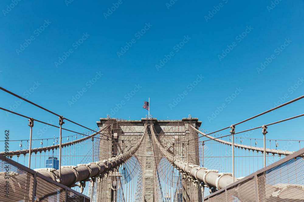 Fototapeta premium brooklyn bridge with american flag on clear blue sky background, new york, usa