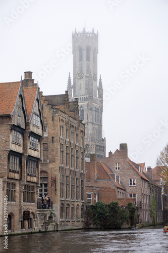 Tourists doing boat trip on canal of Bruges surrounded by flemish buildings in Belgium