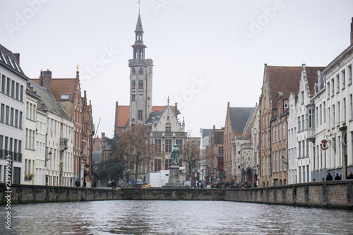 Tourists doing boat trip on canal of Bruges surrounded by flemish buildings in Belgium