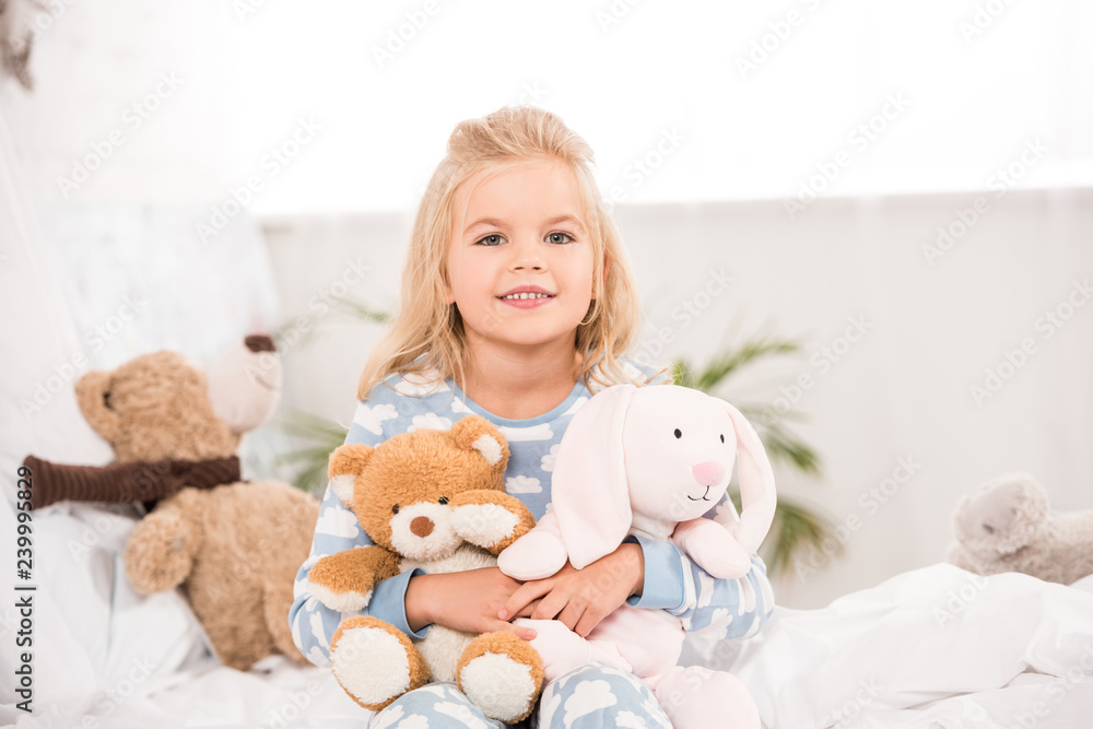 smiling adorable child sitting with soft toys on bed smiling adorable child sitting with soft toys on bed