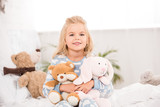 smiling adorable child sitting with soft toys on bed