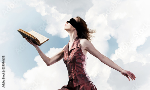 Girl against cloudy sky with opened book in palm as idea for kno
