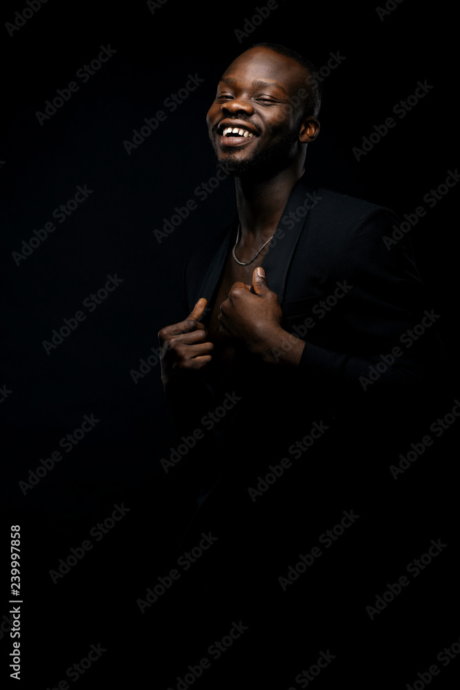 Dark key portrait of handsome smiling male model wearing black jacket and with chainlet on neck. Total black style