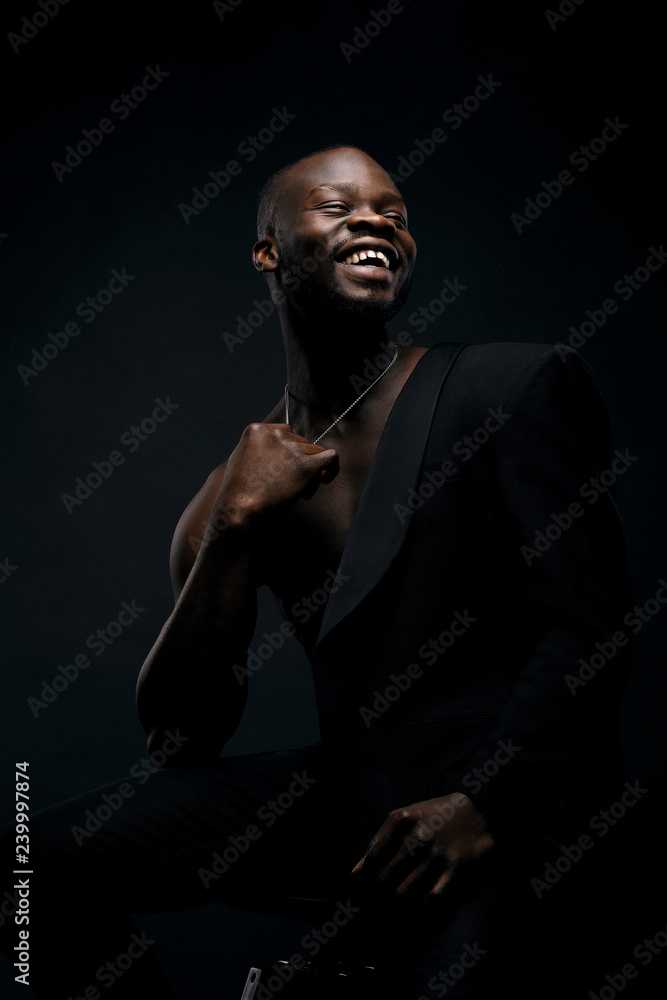 Obraz premium Dark key portrait of handsome smiling male model wearing black jacket and with chainlet on neck. Total black style
