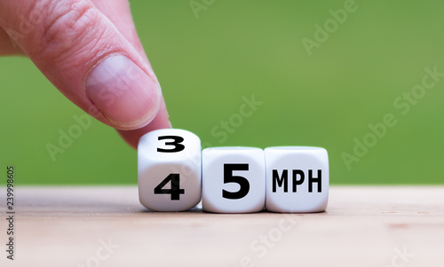 Hand is turning a dice and changes the expression "45 MPH" to "35 MPH" as symbol to reduce the speed limit from 45 to 35 miles per hour