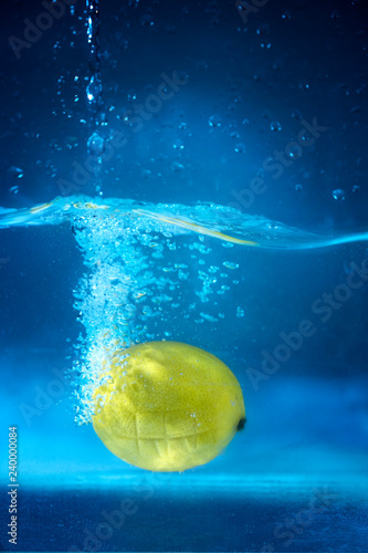Lemon falls into water with splashes and bubbles, on blue background. © Yury