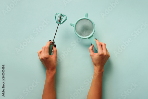 Woman hand holding kitchen utensils on blue background. Baking tools - brush, whisk, spatula. Bakery, cooking, healthy homemade food concept. Copy space