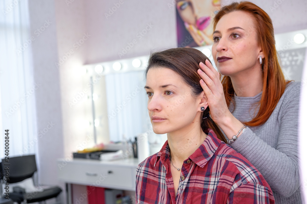 girl makeup artist in the gray shirt doing makeup for the other girl in the red plaid shirt at the beauty salon girl makeup artist in the gray shirt doing makeup for the other girl in the red plaid shirt at the beauty salon