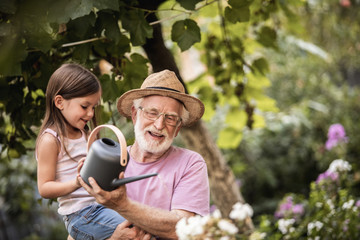 Little girl helping her grandpa watering plants